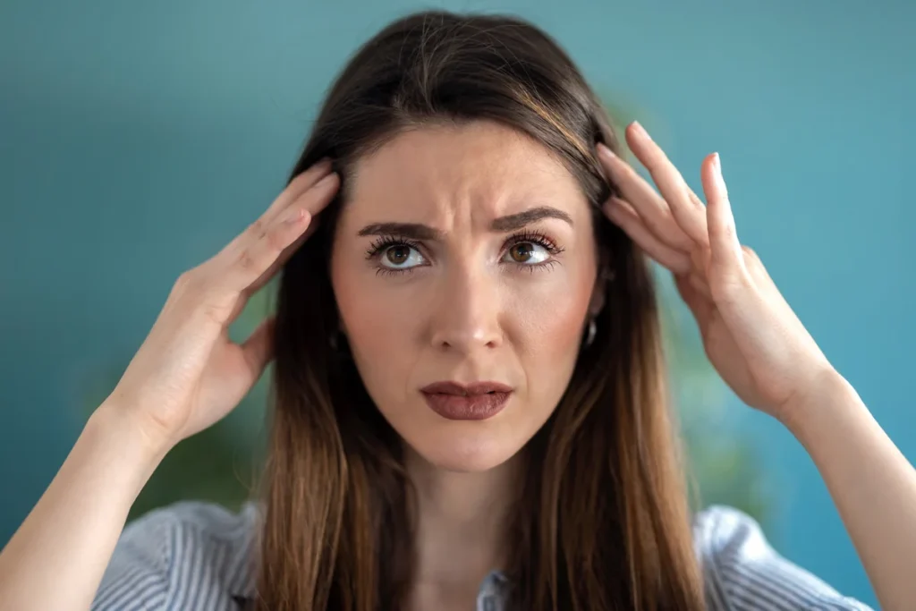 Vrouw met hoofdpijn houdt haar handen tegen haar slapen en fronst